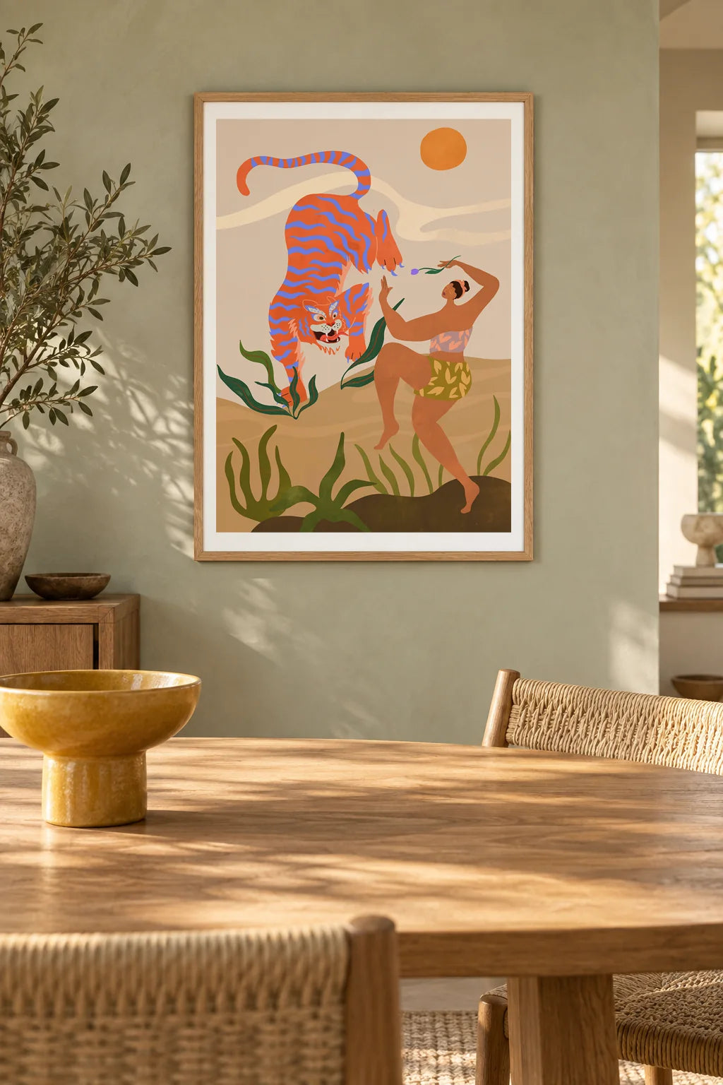 Dance With Me by Arty Guava – orange tiger with violet stripes beside a dancing woman and green leaves. Oak-framed print above a dining table in a sunlit sage room.