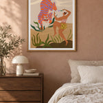 Dance With Me by Arty Guava – orange tiger with violet stripes beside a dancing woman and green leaves. Oak-framed print styled above a walnut bedside chest in a warm bedroom.