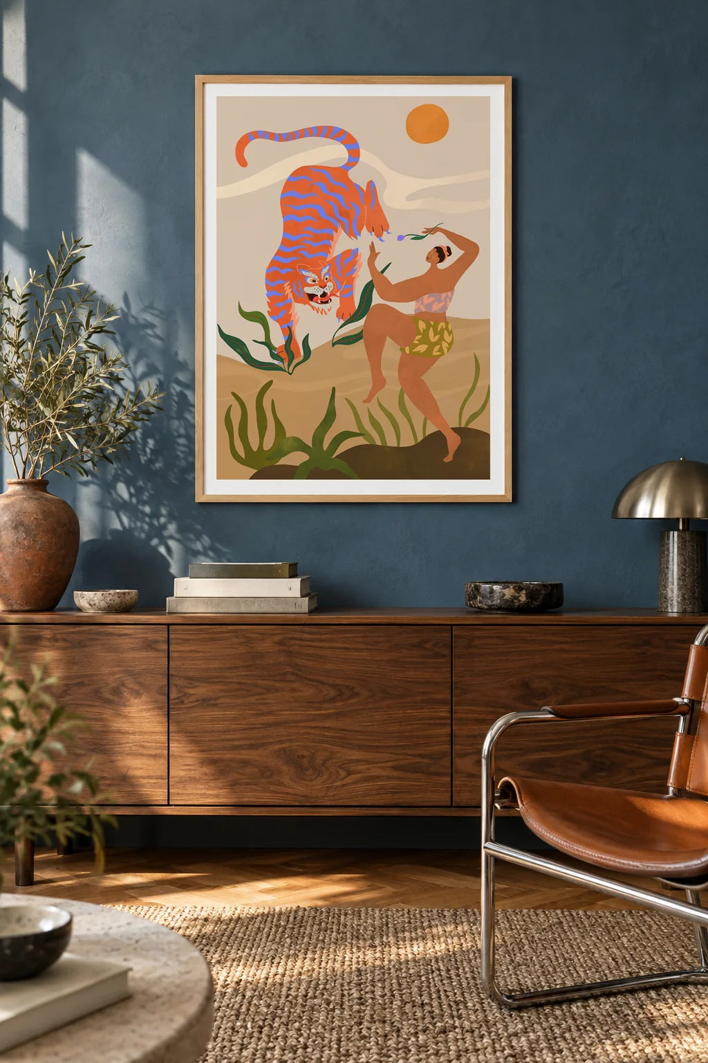 Dance With Me by Arty Guava – orange tiger with violet stripes beside a dancing woman and green leaves. Oak-framed print above a walnut sideboard against a blue living-room wall.