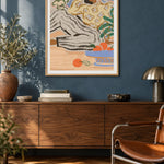 Lazy Days by Arty Guava – reclining woman in a floral blouse beside a blue bowl of oranges. Oak-framed print above a walnut sideboard against a blue living-room wall.