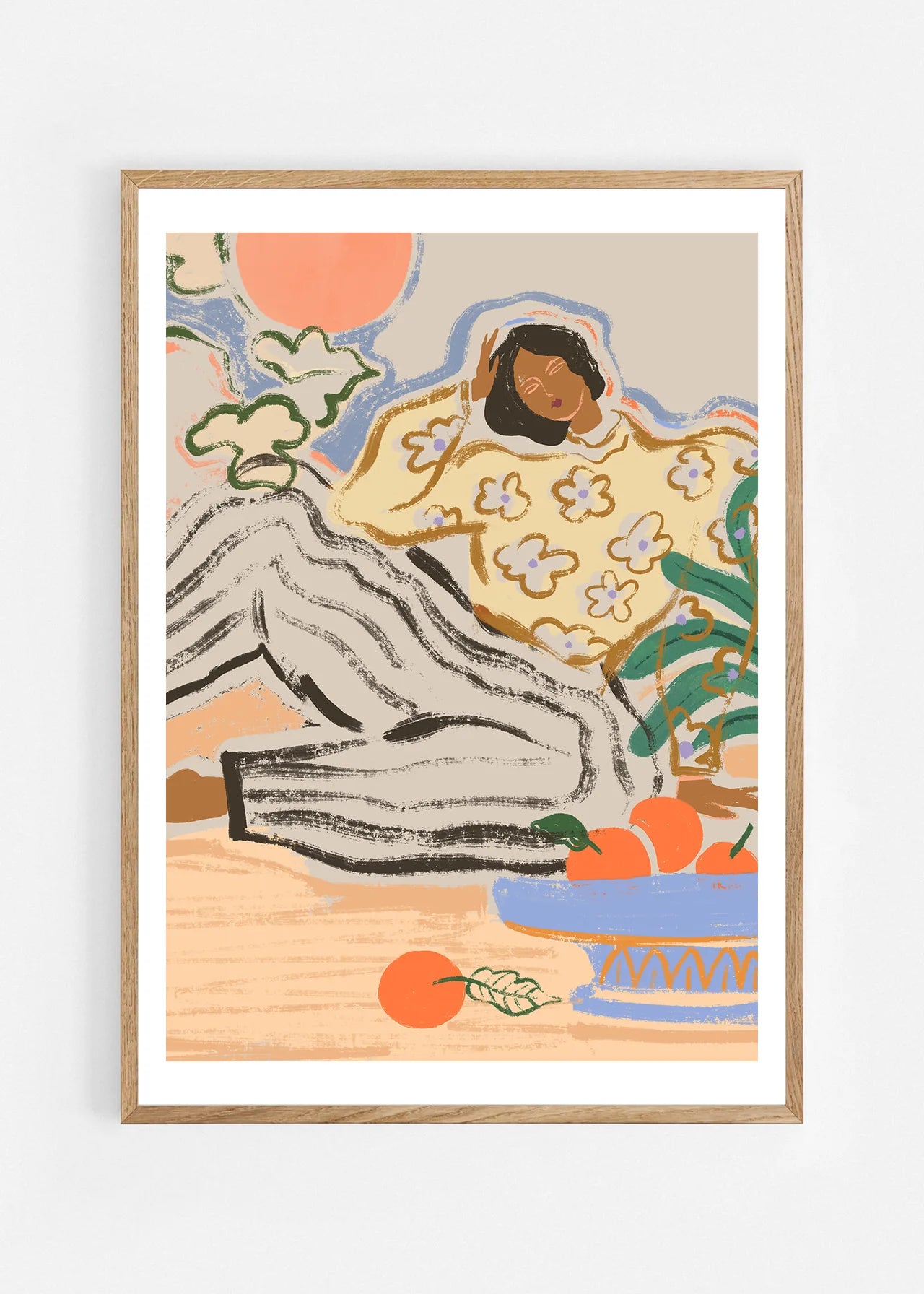 Lazy Days by Arty Guava – reclining woman in a floral blouse beside a blue bowl of oranges. Art print shown in a natural oak frame on a white wall.